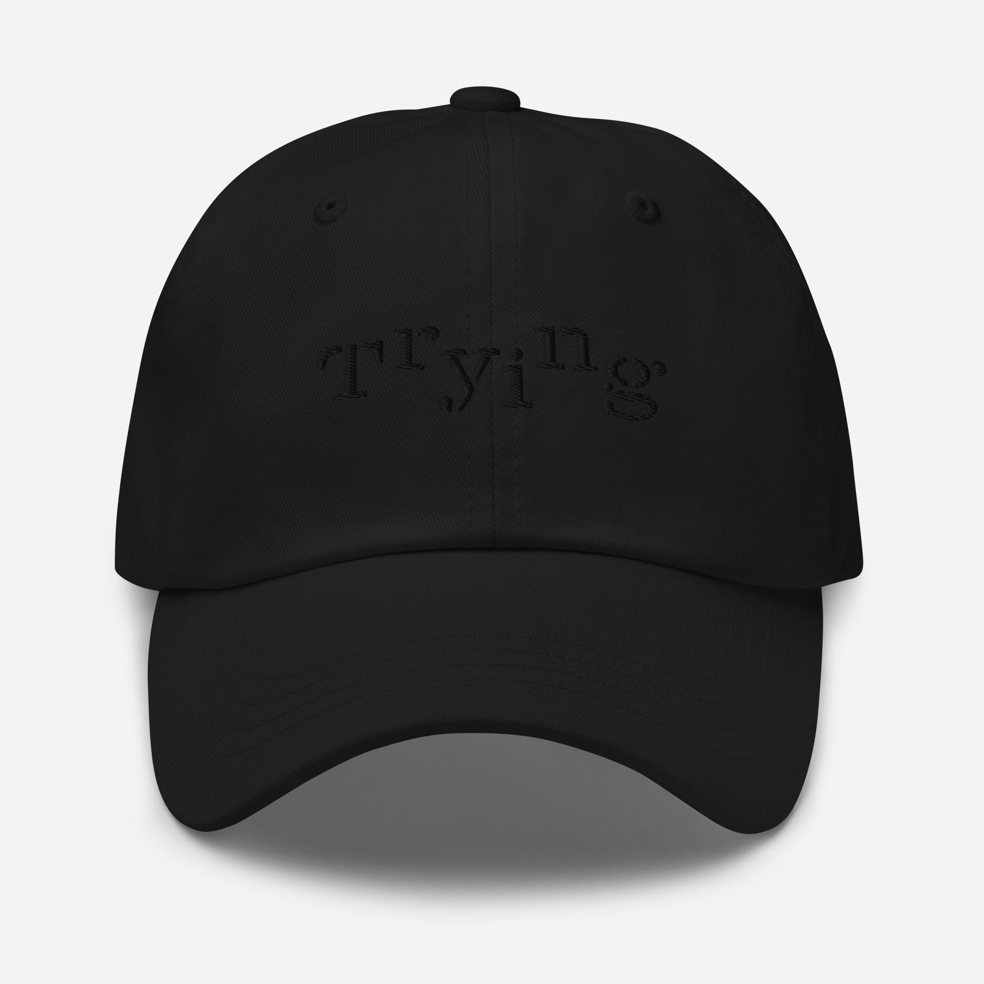 Black classic dad hat with black embroidered text that reads ‘Trying,’ designed by queer creators to express mental health and perseverance. Front view, not on model.