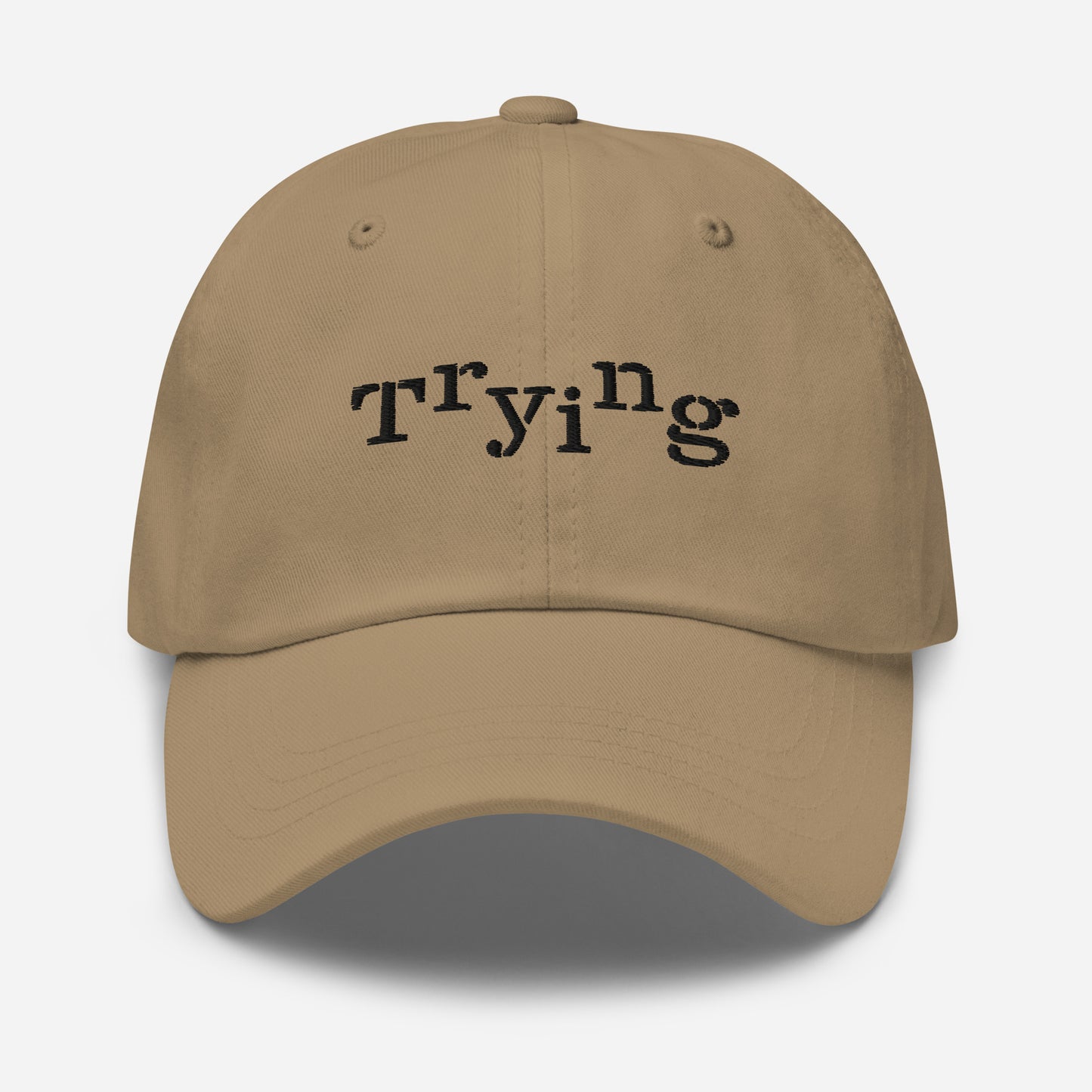Khaki classic dad hat with black embroidered text that reads ‘Trying,’ designed by queer creators to express mental health and perseverance. Front view, not on model.