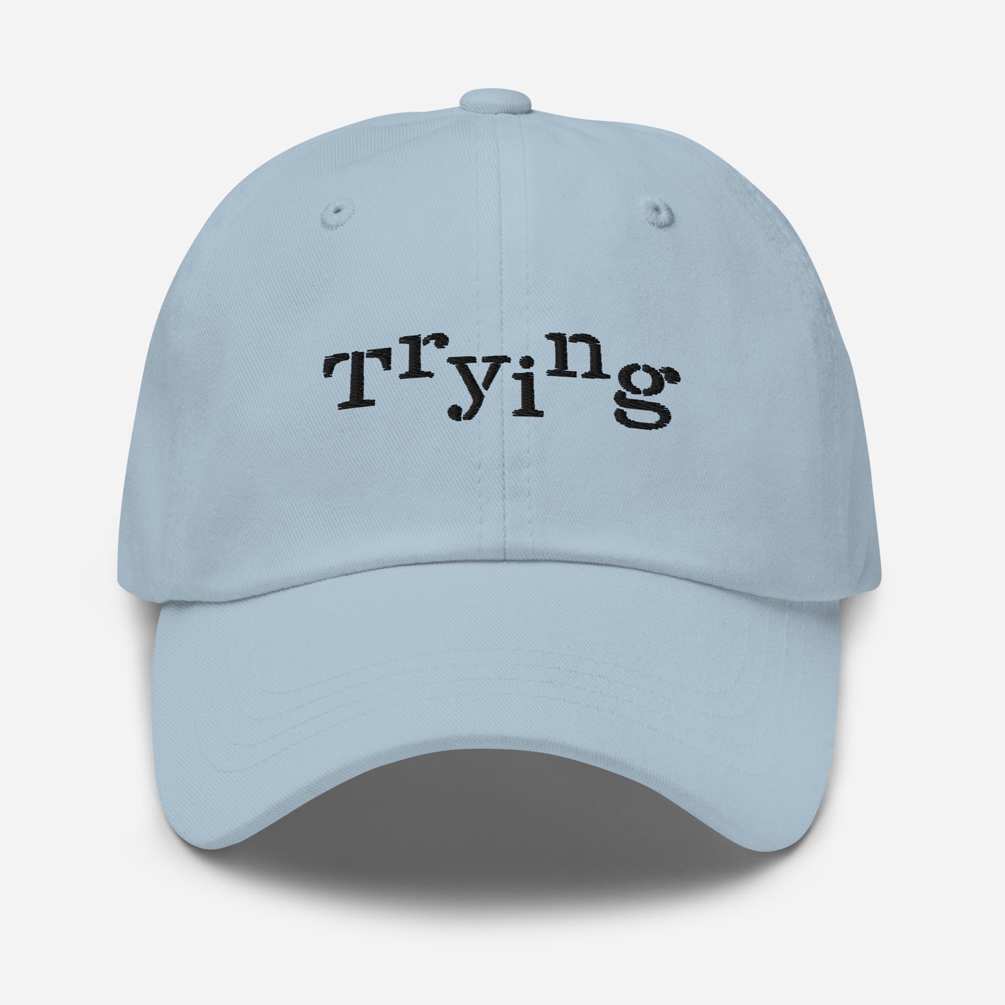 Light blue classic dad hat with black embroidered text that reads ‘Trying,’ designed by queer creators to express mental health and perseverance. Front view, not on model.