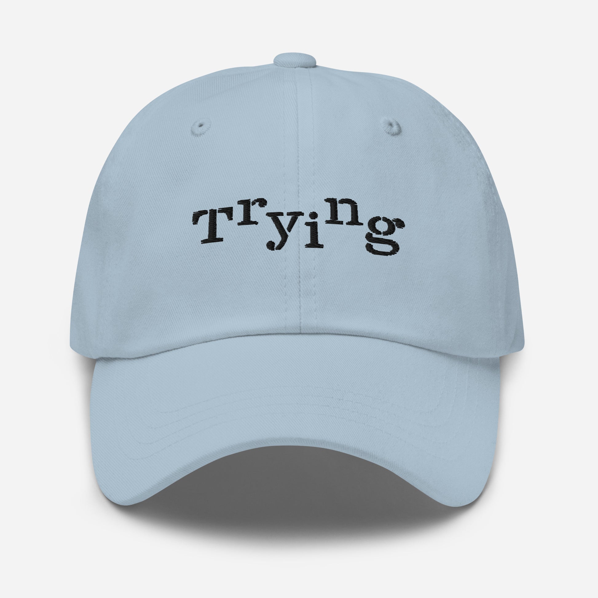 Light blue classic dad hat with black embroidered text that reads ‘Trying,’ designed by queer creators to express mental health and perseverance. Front view, not on model.