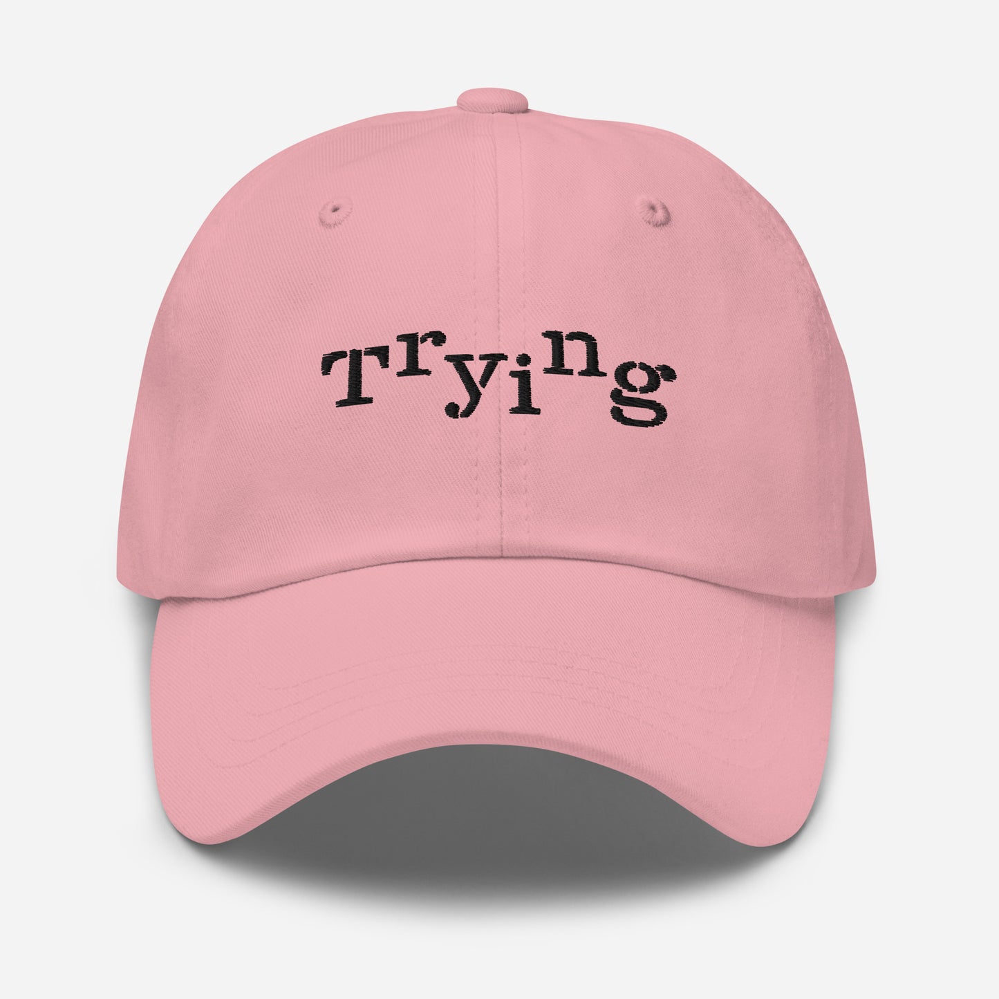 Pink classic dad hat with black embroidered text that reads ‘Trying,’ designed by queer creators to express mental health and perseverance. Front view, not on model.