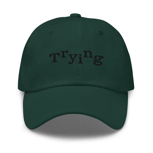 Spruce classic dad hat with black embroidered text that reads ‘Trying,’ designed by queer creators to express mental health and perseverance. Front view, not on model.
