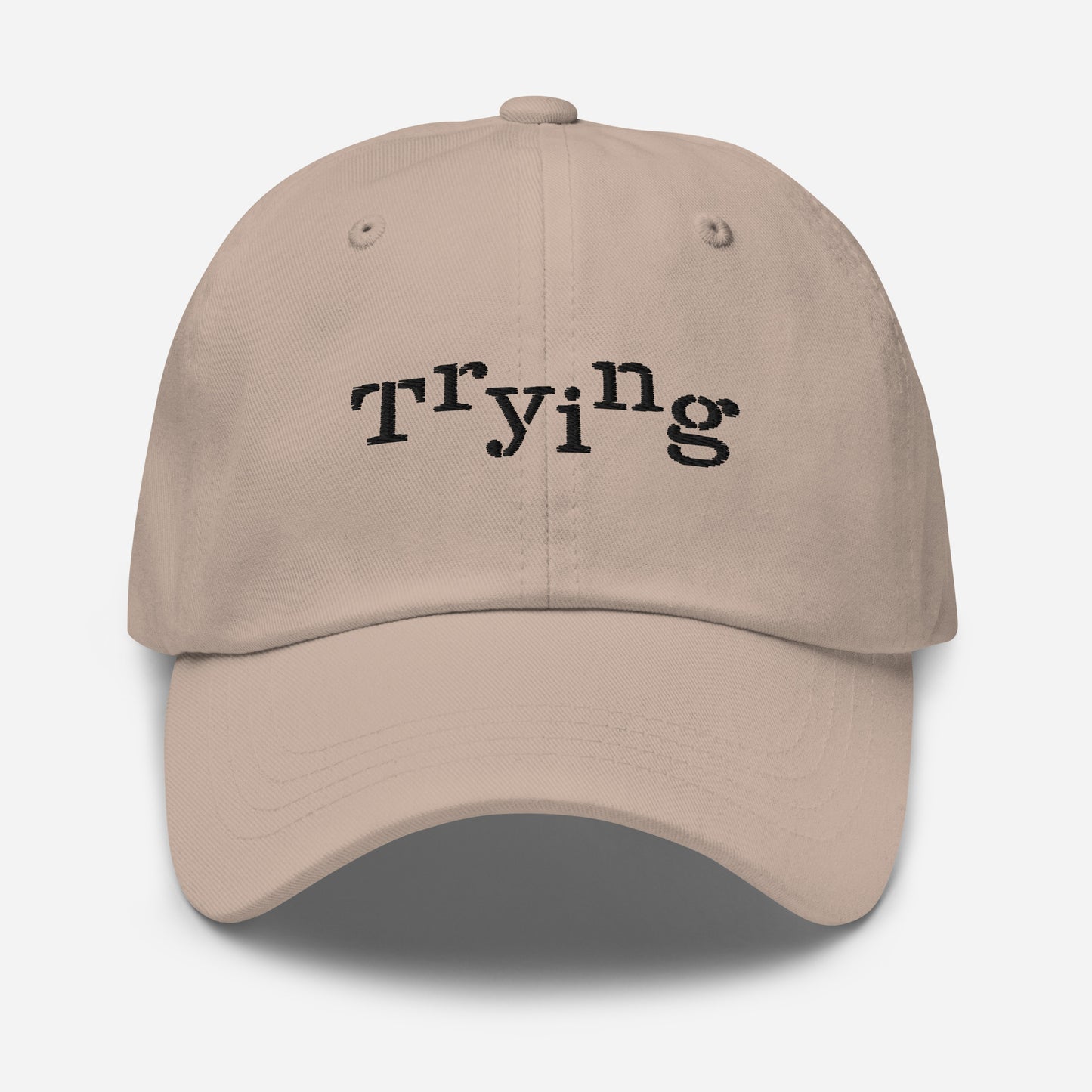 Stone classic dad hat with black embroidered text that reads ‘Trying,’ designed by queer creators to express mental health and perseverance. Front view, not on model.