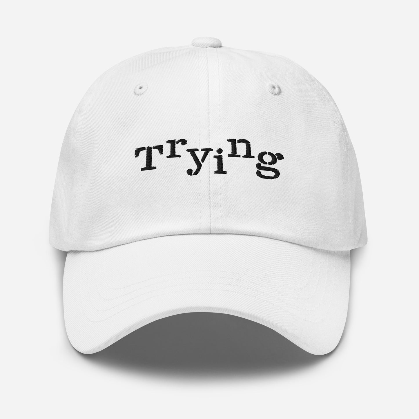 White classic dad hat with black embroidered text that reads ‘Trying,’ designed by queer creators to express mental health and perseverance. Front view, not on model.