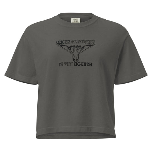 Pepper, boxy t-shirt. Featuring the phrase ‘Queer existence is the agenda’ on the front, ‘here to stay’ on the back. Design is in black, with a butterfly design on the front and an abstract design on the back. Design is in contrast to legislation that is based on eraser of queer people. Designed by a small LGBTQ+ owned business. Front of shirt. 