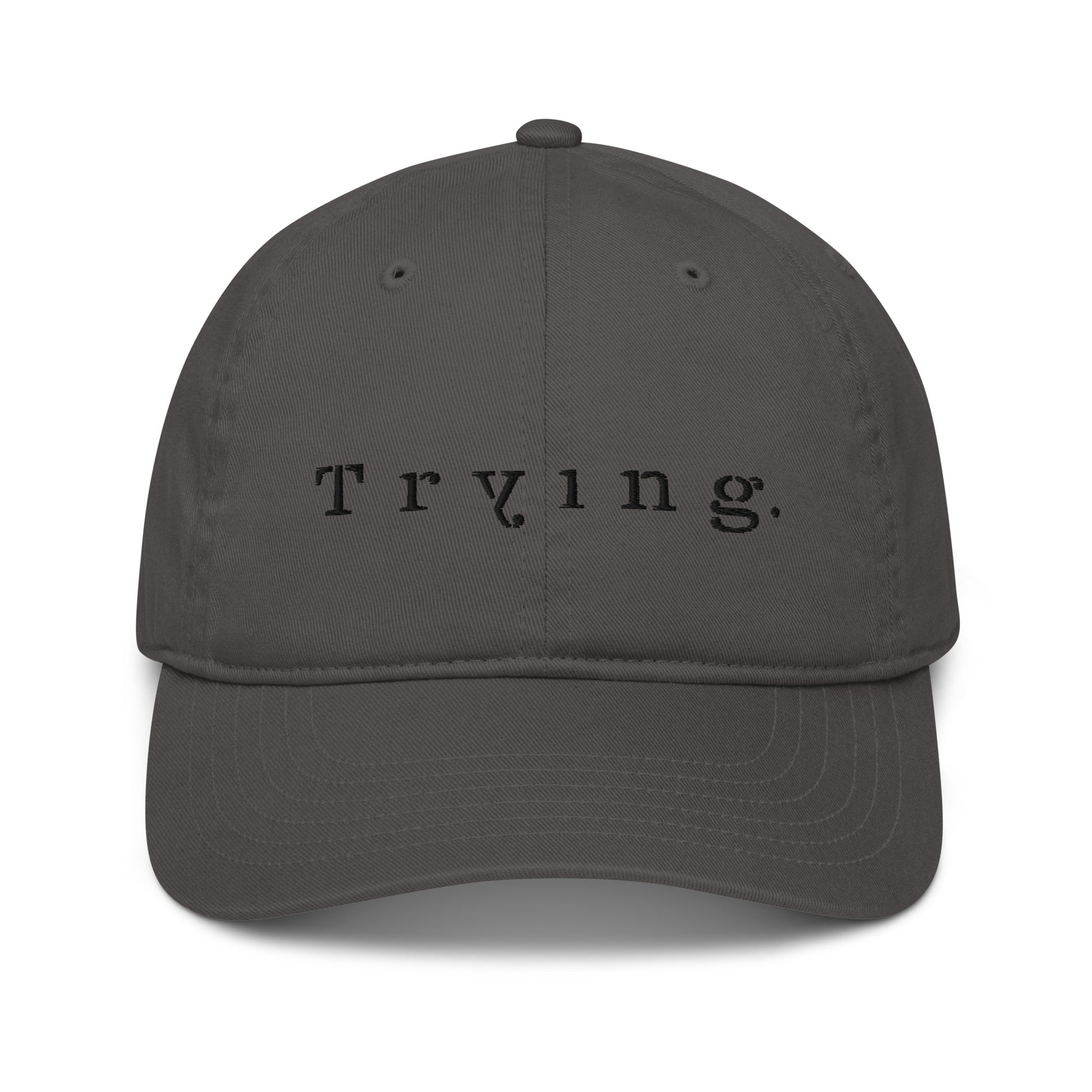 Charcoal dad hat embroidered with the word "Trying." in spaced serif lettering — a 12:AM Intuition design honoring the messy middle. 
