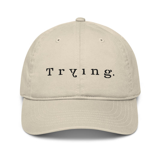 Stone dad hat embroidered with the word "Trying." in spaced serif lettering — a 12:AM Intuition design honoring the messy middle.